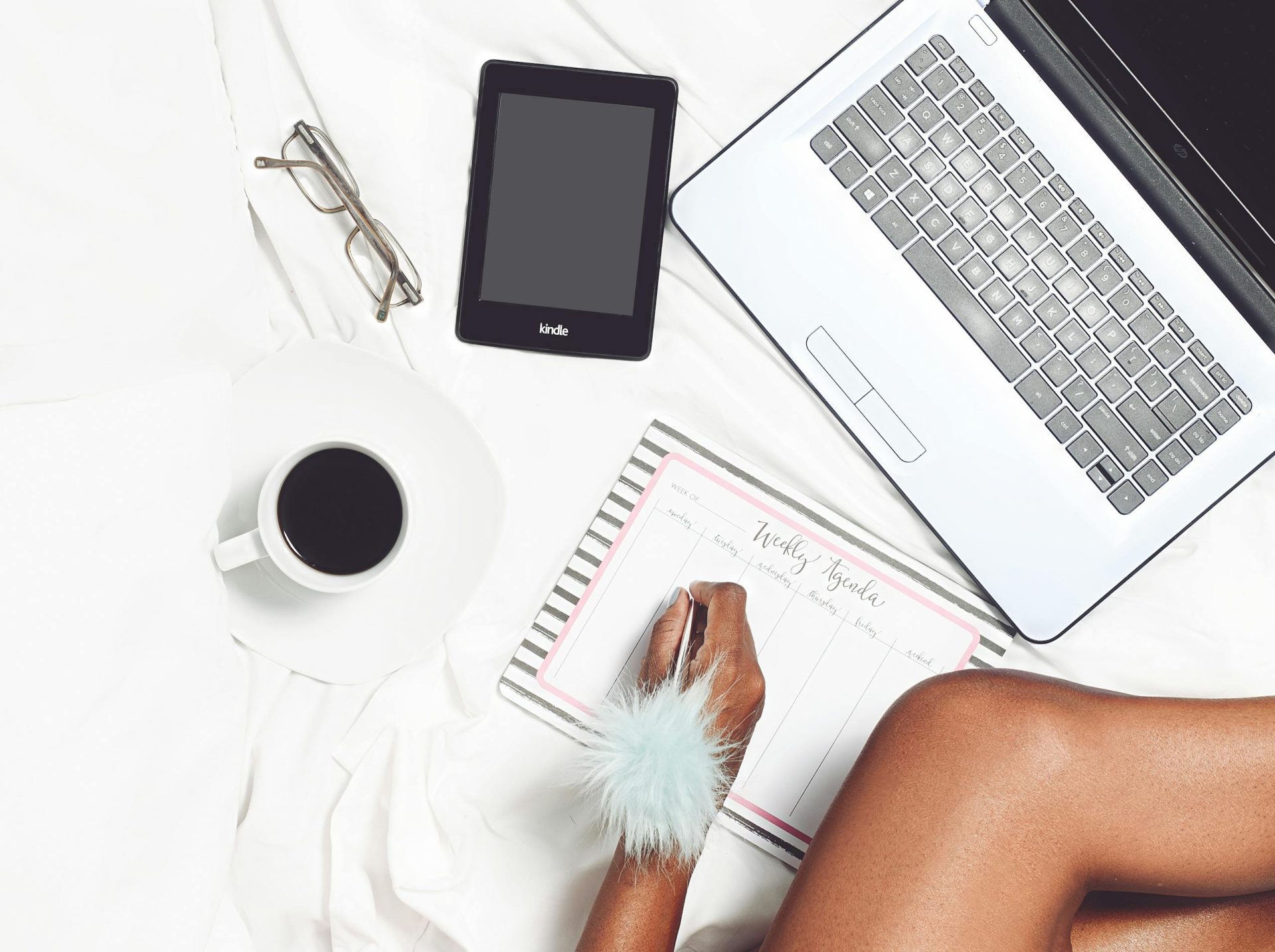 Flat lay of a cozy workspace with a coffee cup, laptop, Kindle, and planner for productivity.